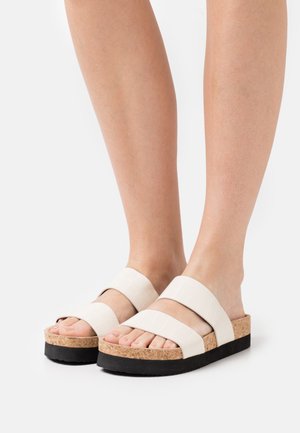 Hvide faux-krokodille-lædersandaler med to brede remme, kork-mellemsål og sort gummiydersål; åben tå-design med teksturerede detaljer.