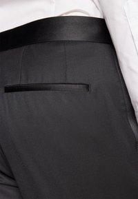 Calças pretas de fato com uma textura elegante e suave. Apresentam uma cintura em cetim e um bolso traseiro discreto com acabamento em cetim.