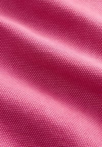 Gros plan d’un tissu rose lisse et étroitement tissé montrant un petit tissage texturé régulier et de doux plis.
