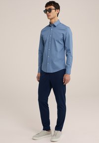 Svetlo modra srajca s dolgimi rokavi, v kombinaciji s temno modrimi hlačami in svetlo sivimi supergami. Model nosi črne sončne očala.