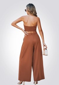 Top court en tricot marron et pantalon large avec un design texturé. Les accessoires comprennent un petit sac à main blanc et des lunettes de soleil.
