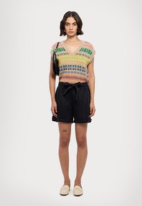 Tricou tricotat cu modele multicolore, de tip v, și mâneci scurte; asortat cu pantaloni scurți negri, largi și pantofi slip-on.
