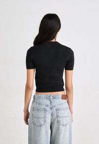 Svart, tettsittende kortermet strikket topp med rund hals, kombinert med lyseblå, høyt liv jeans med et lærmerke bak.