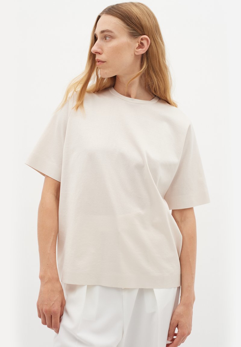 T-shirt corto a maniche corte color beige chiaro in un morbido misto cotone, con scollatura rotonda e vestibilità comoda, caratterizzato da una texture liscia e minimale.