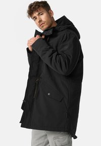 Parka noire avec capuche, dotée d'une fermeture éclair, de poches latérales et de cordons de serrage réglables. Fabriquée en tissu durable avec une finition mate.