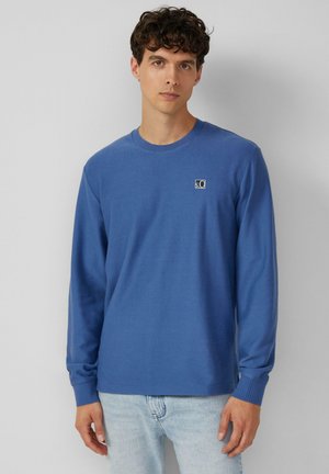 Langsleeve blauwe shirt van gebreide stof, met een ronde halslijn en een klein logo op de linkerkant van de borst. Getailleerd bij de manchetten.