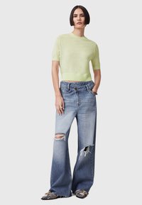 Lichtgroen, mouwloos, cropped top van gebreid materiaal, gecombineerd met versleten, wijde blauwe spijkerbroek met scheuren.