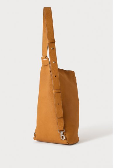 Sac à bandoulière en cuir fauve avec sangle réglable et fermoir métallique, debout sur un fond clair uni.