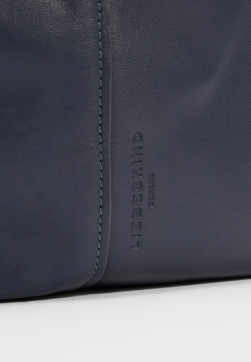 Dunkelnavy Lederhandtasche mit glatter Textur, filigraner Stichung und geprägtem Markenlogo. Minimalistisches Design mit klaren Linien.