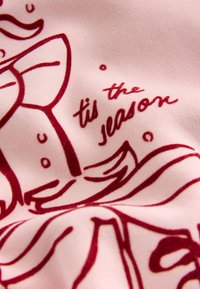 Ružová textília má červený potlačený vzor špirál a text "tis the season" s hladkou textúrou a výraznými obrysmi.