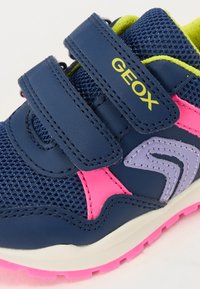 Scarpa atletica blu con accenti rosa e viola, realizzata in materiali mesh e sintetici. Dotata di cinturini in Velcro e suola texture.