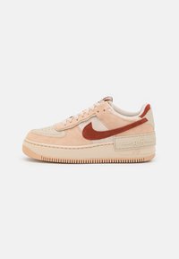 Nike Air Force 1 sneakers in light peach suede with brown accents. Features a textured outsole and padded collar for comfort.