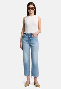 Débardeur blanc à côtes, jean taille haute bleu clair avec ourlet effiloché, escarpins jaunes à motif serpent, et lunettes de soleil rectangulaires sombres.