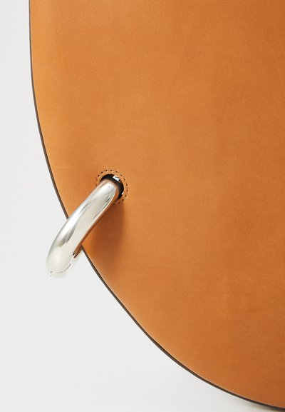 Sarkana ādas soma ar gludu tekstūru, kurai ir sudraba metāla rokturis, piestiprināts caur apaļu atveri, un akcentēta ar kārtīgu šuvumu.