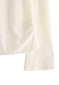 Weißes, texturiertes Blusenshirt mit einem zarten Blumenmuster, langen Ärmeln mit gerafftem Detail an der Schulter und geradem Saum.
