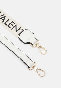 Canvas strap in beige with black lettering, featuring white leather accents and gold-tone metal clips. Smooth texture, flat design.