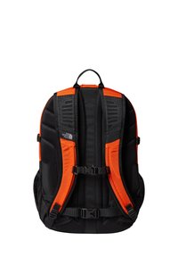 Czarny i pomarańczowy plecak z wyściełanymi siateczkowymi paskami, regulowanymi klamrami i zaprojektowany w sposób strukturalny, aby zapewnić ergonomiczne wsparcie.