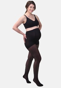 Collants de maternité noirs avec une texture lisse et extensible, conçus pour s'adapter à un ventre en croissance, dotés d'une taille haute et d'un design avec pieds.