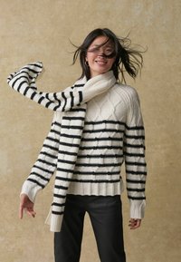 Pull en tricot crème avec un motif en losange texturé et des rayures noires ; accompagné d'une écharpe longue à rayures noires et blanches.