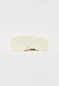 Talpa unei adidaș care prezintă un material din cauciuc texturat, de culoare albă murdară, cu un model zimțat și detaliu cu un logo circular.