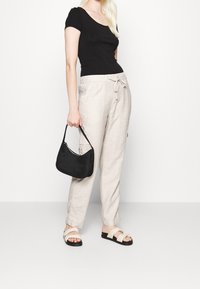 Zwarte getailleerde top, beige linnen broek met strik in de taille, zwarte textuur handtas en zwarte sandalen met crèmekleurige banden. Eenvoudige en ontspannen outfit.