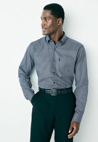 Hosszú ujjú, gombos ing sötétkék alapon geometrikus fehér mintával. Fekete nadrággal és fekete övvel párosítva.