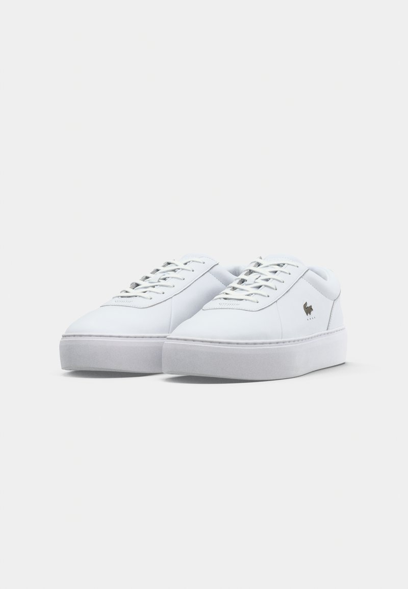 White leather sneakers with rounded toe, lace-up design, and thick white rubber sole. Small logo detail on the outer side. Smooth texture.