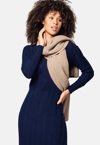 Abito a maglia navy a coste con silhouette aderente e maniche lunghe, sovrapposto a una sciarpa in cashmere beige drappeggiata sulle spalle.