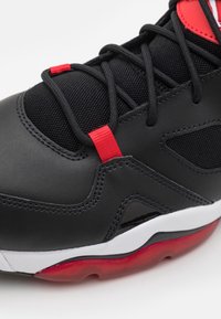 Černá sportovní bota vyrobená z kůže a síťoviny, s červenými akcenty, bílou mezipodešví a viditelným vzdušným polstrem v podešvi.