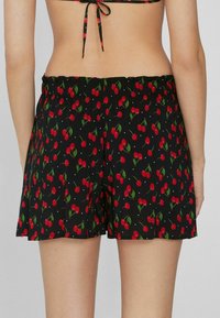 Černé šortky s potiskem červených třešní a zelených listů, s elastickým pasem a volným střihem.