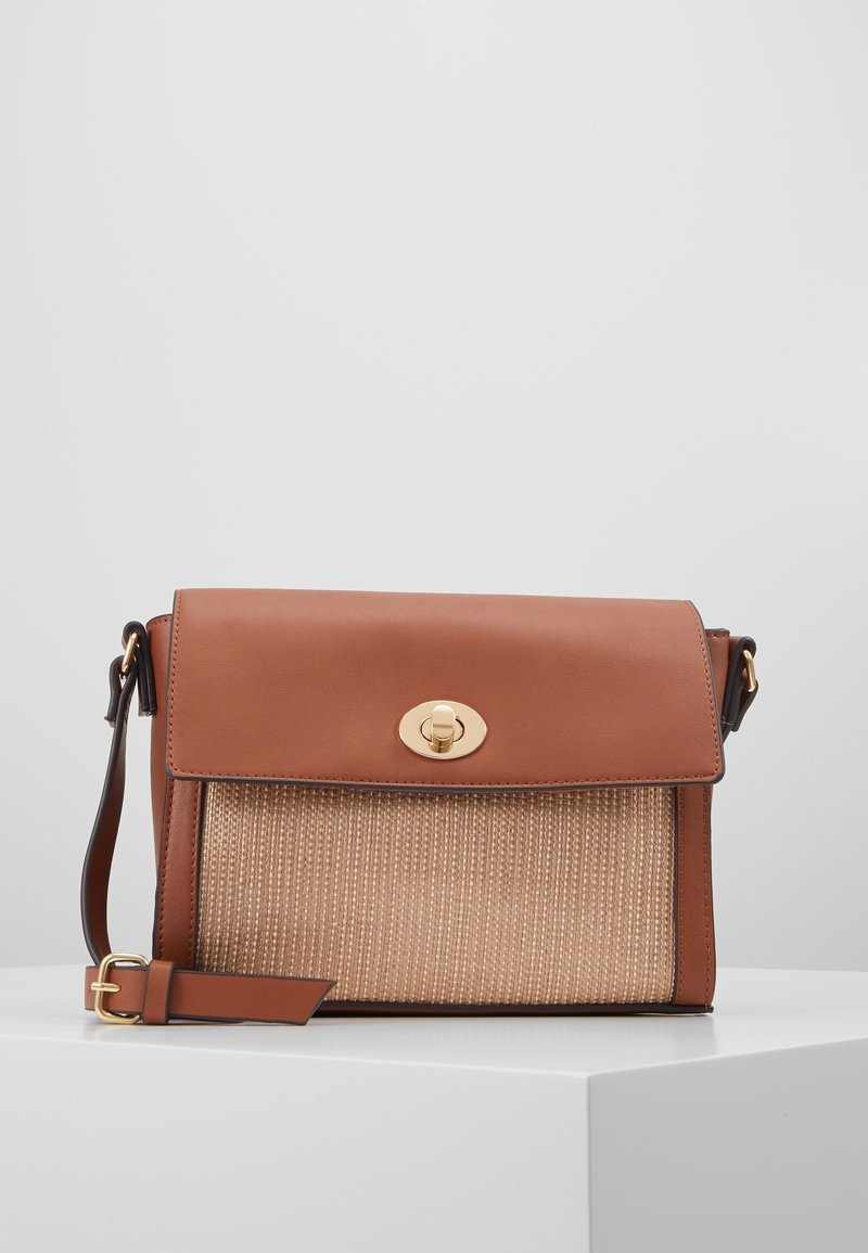 Borsa a tracolla in pelle marrone e rattan intrecciato con chiusura a scatto dorata e tracolla in pelle regolabile su superficie bianca.