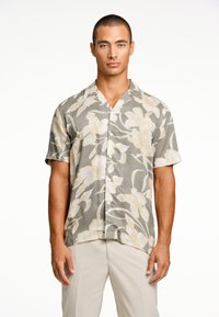 Camisa de botones de manga corta en un fondo gris con grandes patrones florales en color crema, que cuenta con un cuello tipo campamento y una tela ligera.