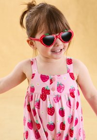 Rochie roz cu model de căpșuni, cu bretele fine și un detaliu cu nasture. Copil purtând ochelari de soare în formă de inimă roșie cu accente verzi.