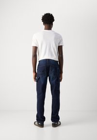 Dark blue denim cargo pants with multiple large pockets, straight leg design, and contrasting stitching, paired with a white t-shirt.