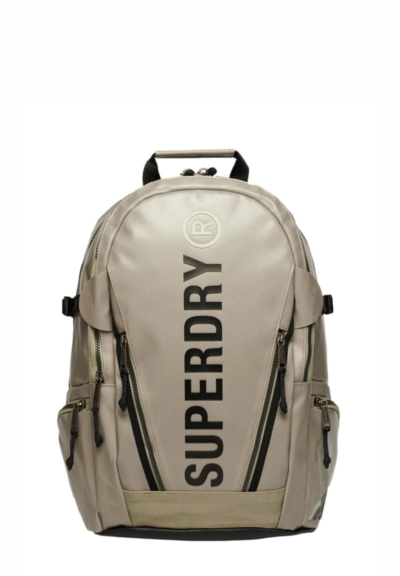 Zaino beige con scritta nera "SUPERDRY", molteplici tasche con zip, materiale in tessuto, spallacci imbottiti e maniglia superiore per il trasporto.