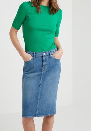 Grünes, figurbetontes Oberteil kombiniert mit einem blauen Denim-Bleistiftrock. Der Rock verfügt über Vordertaschen und eine mittelhohe Taille mit geradem Schnitt.