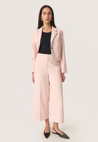 Blush pink skræddersyet blazer og bukser med bredt ben, parret med en sort ribbet top. Glat tekstur, enknapslukning på blazeren.