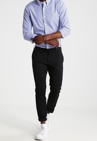 Blue and white striped button-up shirt, black slim-fit trousers, and white sneakers. Shirt features a logo, pants and shoes have a smooth finish.