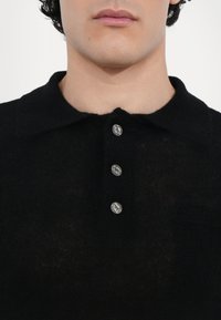Czarny, dziany polo z usztywnionym kołnierzykiem, pięcioma srebrnymi guzikami i miękką fakturą. Brak widocznych wzorów lub logo.