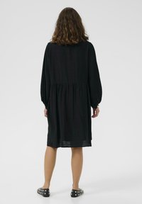 Rochie neagră cu mâneci lungi și talie ajustată, având un detaliu plisat în spate. Pur și simplu cu pantofi negri cu tinte.