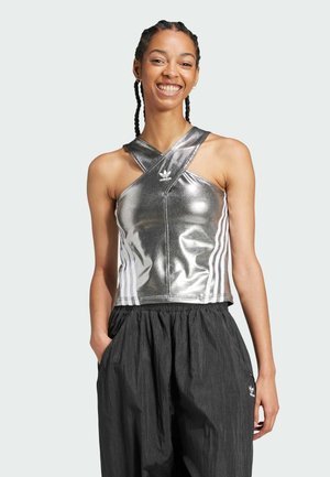 Top corto metallico argento con scollatura incrociata, caratterizzato dal logo Adidas, abbinato a pantaloni neri morbidi. Tre righe bianche sui lati.