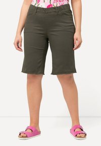 Olivově zelené bermudy s elastickým pasem, délky po kolena, se třepeným lemem. V kombinaci s růžovými skládacími sandály.