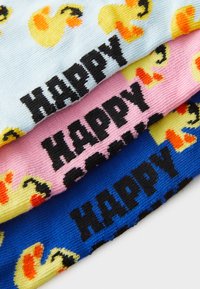 Drie paar sokken in blauw, roze en lichtblauw. Elk paar heeft gele eendontwerpen en het woord "HAPPY" in het zwart.
