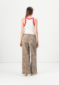 Débardeur blanc avec bordure rouge associé à un pantalon large beige à motif léopard. Tissu lisse et coupe décontractée, chaussures décontractées.