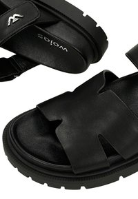 Czarne skórzane sandały z odkrytymi palcami, grubą podeszwą z bieżnikiem oraz szerokimi paskami z wycięciami i regulowanym paskiem z tyłu.