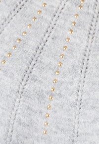 Suéter gris de punto con filas verticales de pequeños adornos en tono dorado, con una tela texturizada y patrones de costura distintivos.
