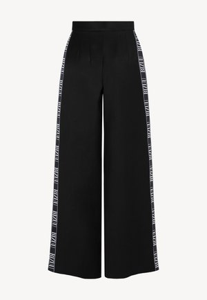 Czarne spodnie o szerokich nogawkach z wysokim stanem i białymi paskami z logo biegnącymi pionowo wzdłuż zewnętrznych stron obu nóg.