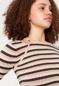 Top de manga longa com nervuras, apresentando riscas horizontais alternadas em preto, branco e bege. Inclui detalhe de alça no ombro e material texturizado.