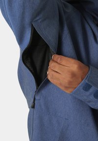 Giacca di jeans blu con tasca con zip e rivestimento nero, polsini regolabili con Velcro e design del colletto strutturato.