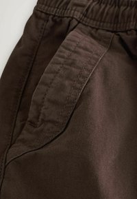 Close-up of dark brown pants showing an elastic waistband and a detailed stitched side pocket.
